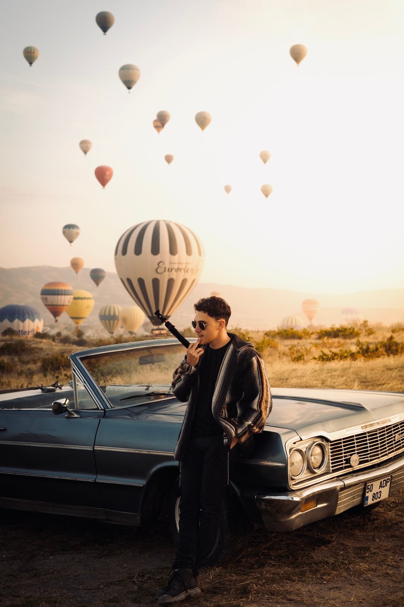 Man leaning on a classic car with hot air balloons rising over Cappadocia