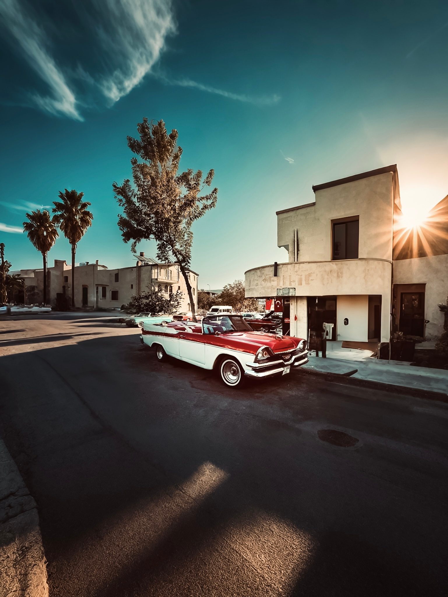 Vintage red convertible parked on a sunlit street with palm trees