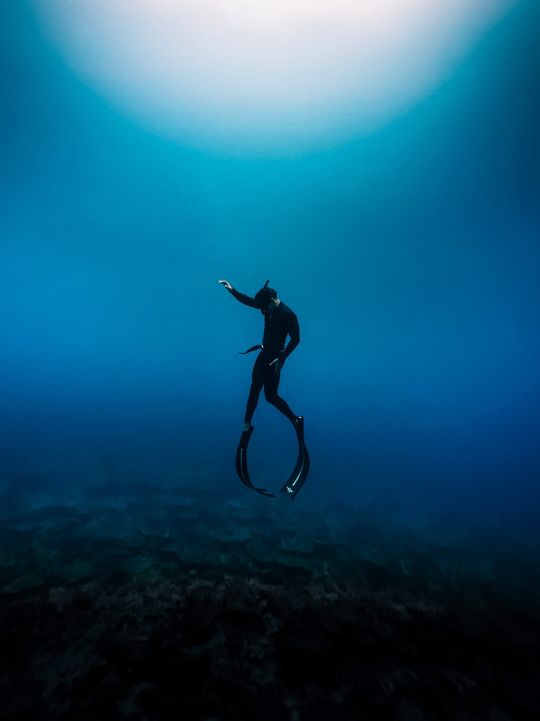 Freediver descending into deep blue water with light from the surface