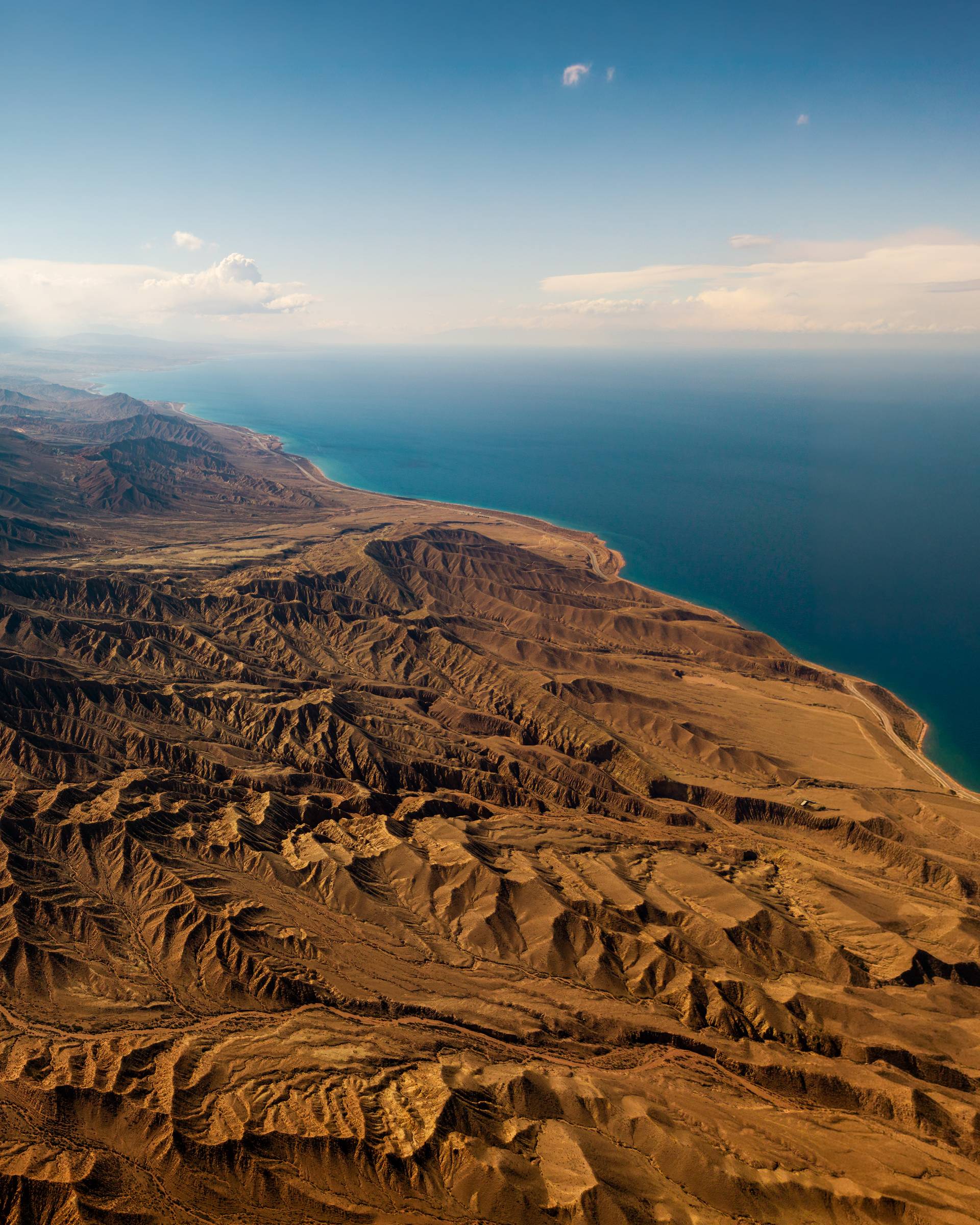 Aerial view of eroded desert hills meeting a deep blue lake, Kyrgyzstan