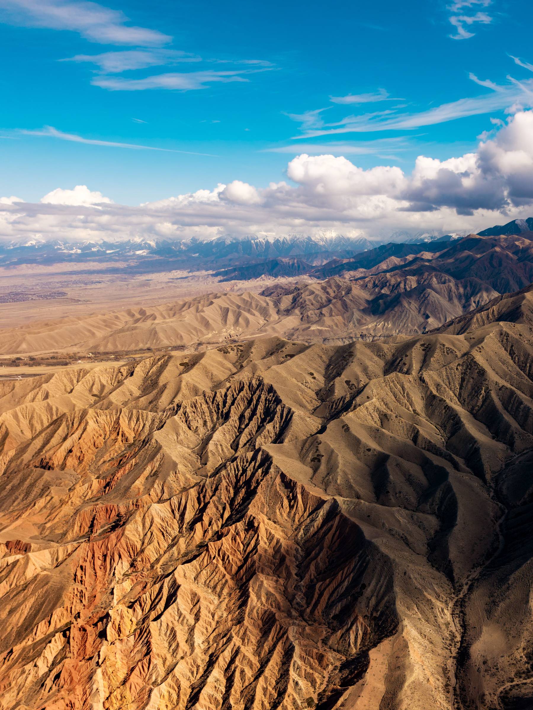Aerial view of rugged red and ochre mountains under a blue sky, Kyrgyzstan