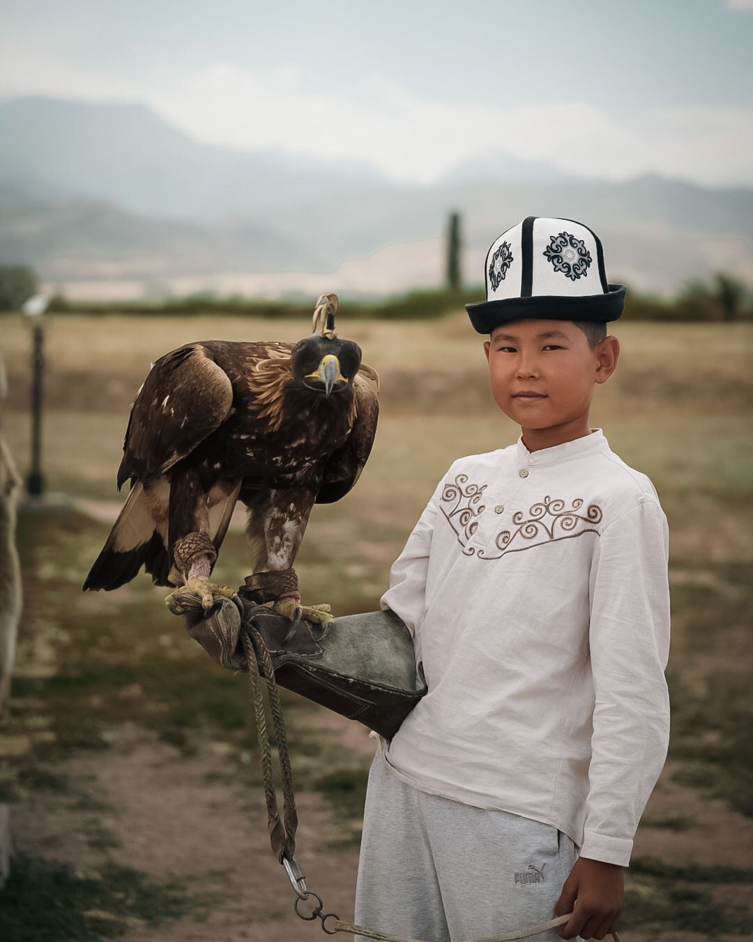 Young eagle hunter in a traditional kalpak holding a golden eagle, Kyrgyzstan