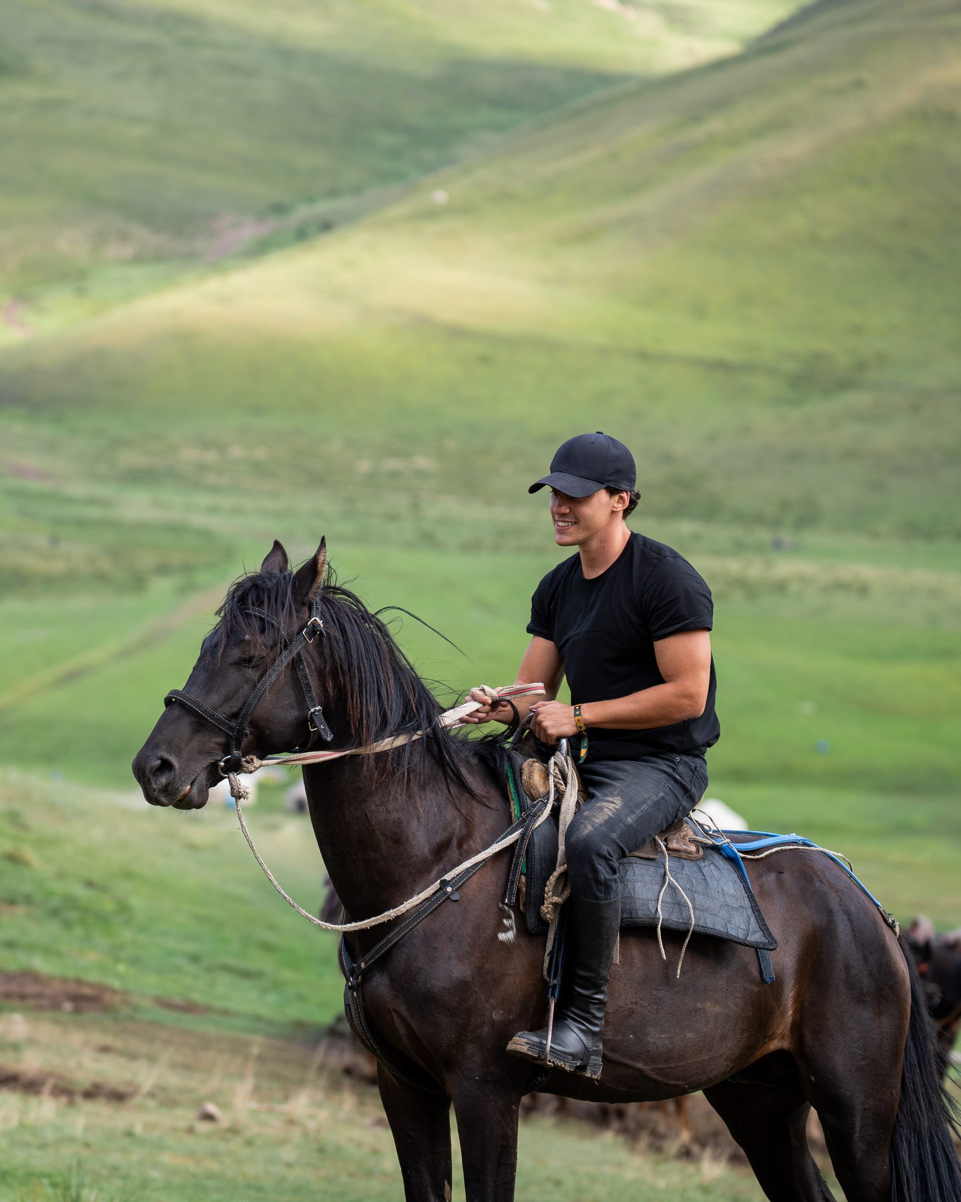 Rider on a dark horse in the green valleys of Kyrgyzstan