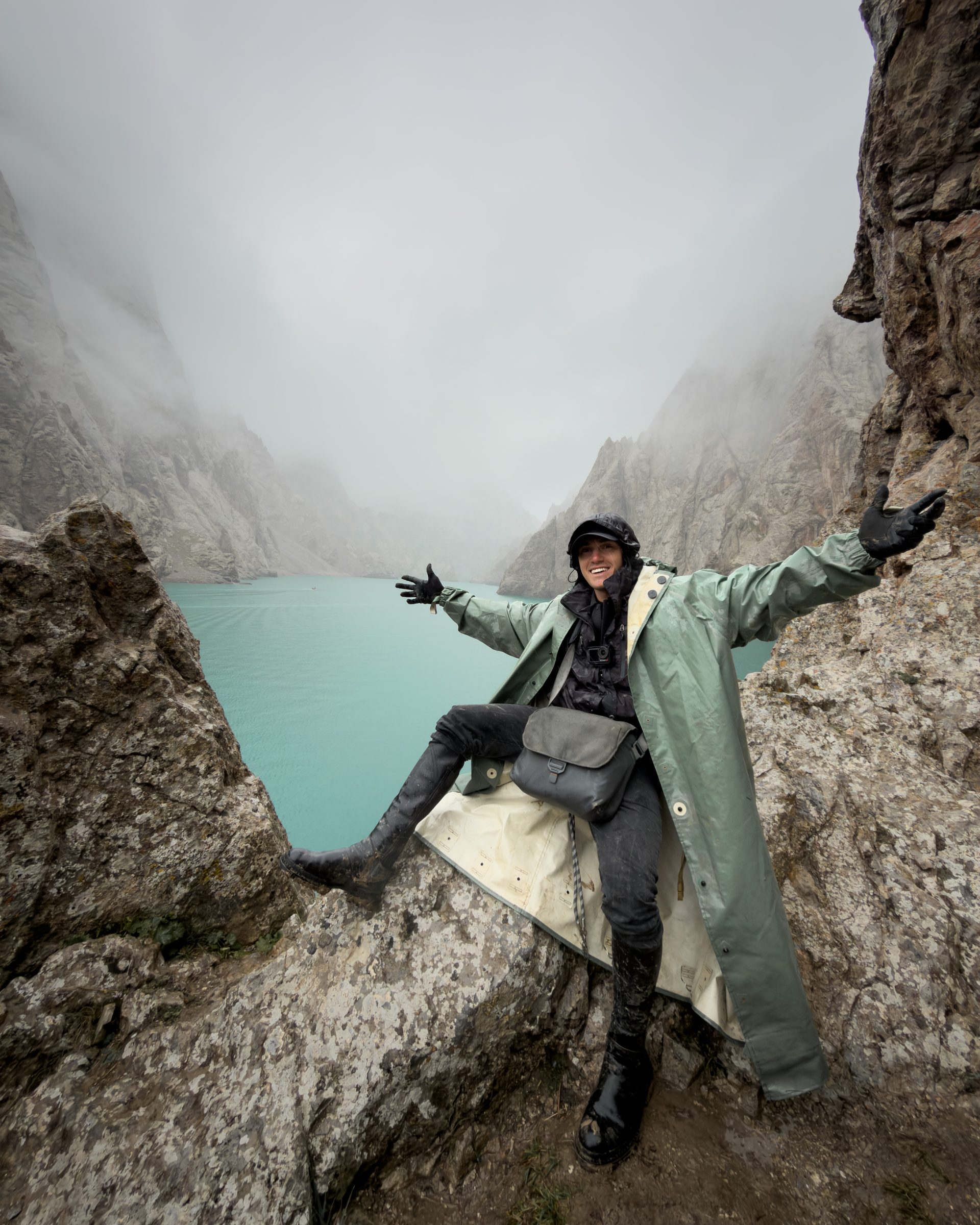 Trekker on a rocky ledge above a turquoise mountain lake in the mist, Kyrgyzstan