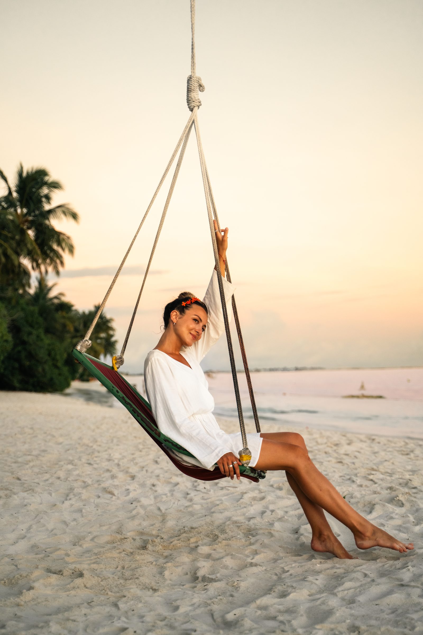 Woman relaxing in a hanging beach swing at sunset, Maldives