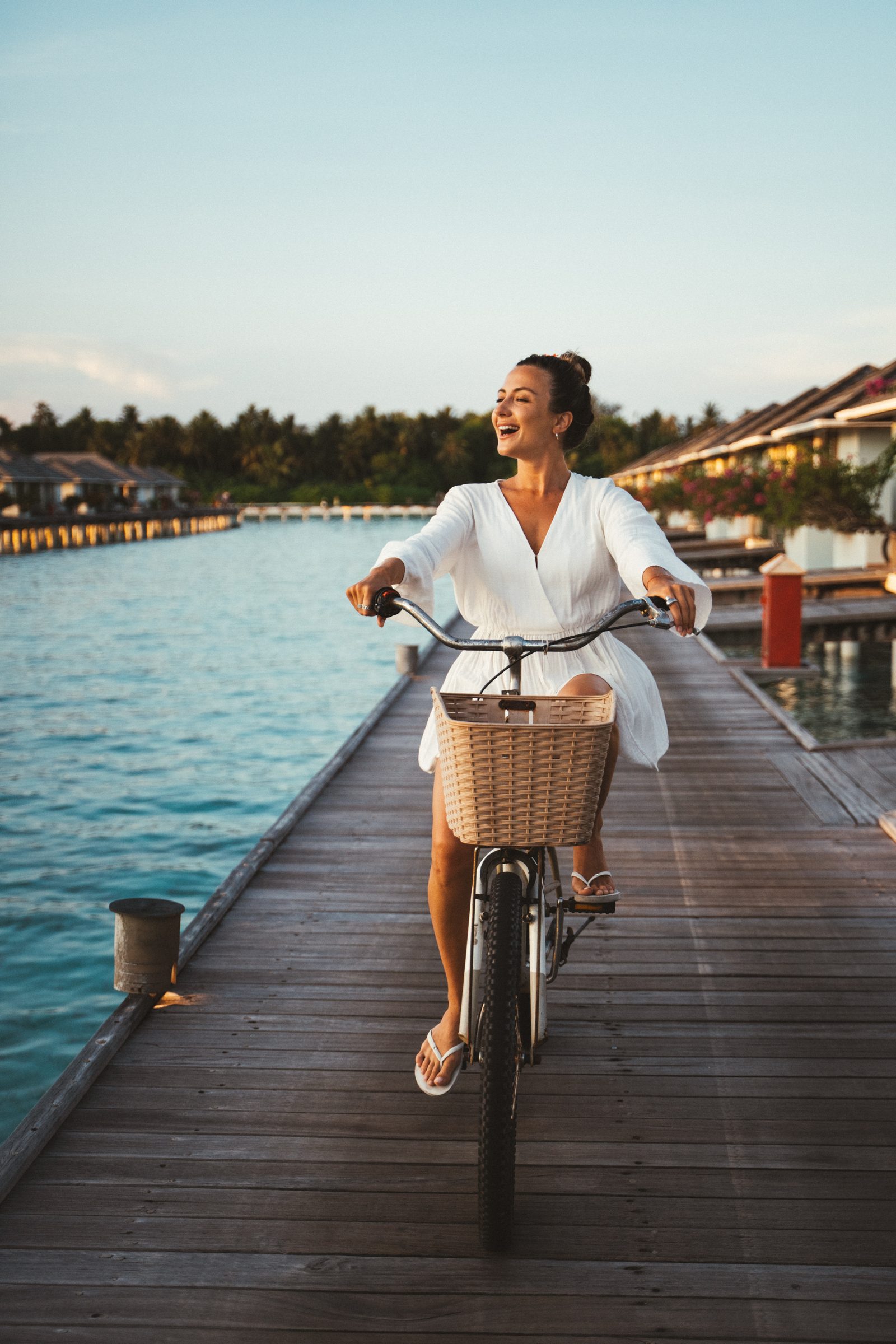 Smiling woman riding a bicycle on a wooden jetty, Maldives resort