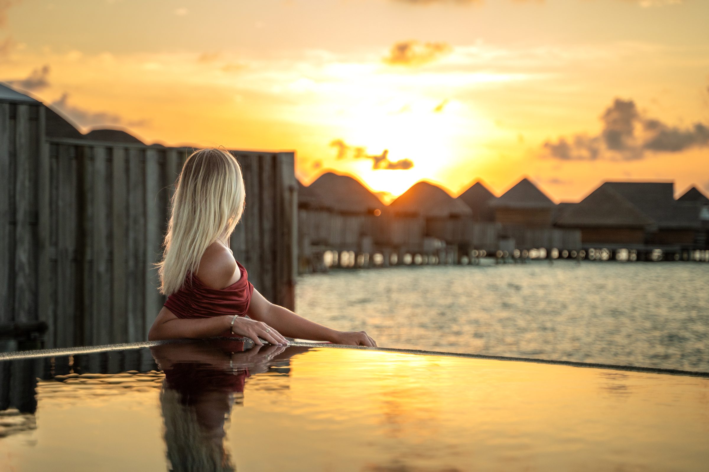 Woman in an infinity pool watching sunset over water villas, Maldives