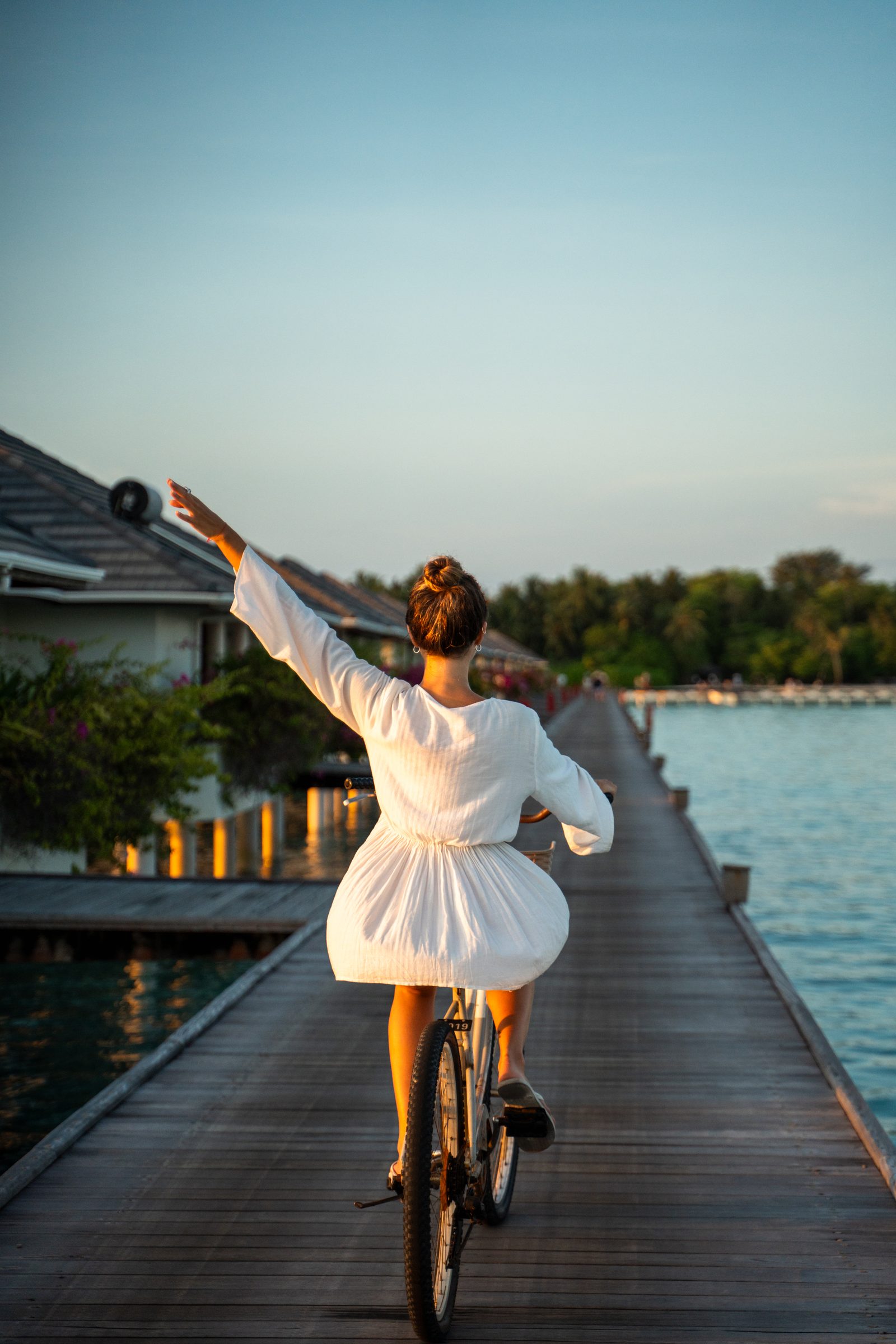 Woman cycling along the jetty between overwater villas, Maldives