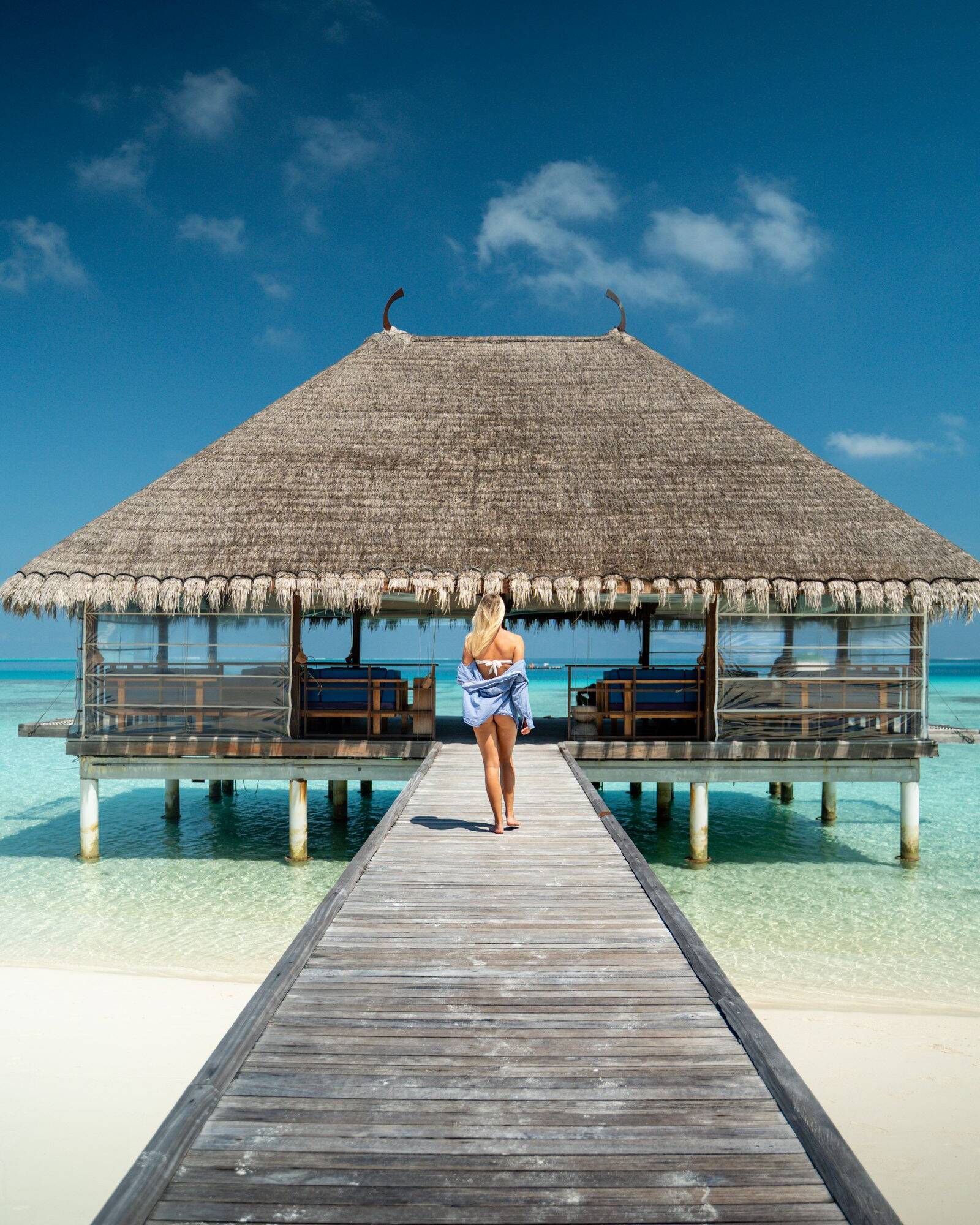 Woman walking down a jetty to a thatched overwater pavilion, Maldives