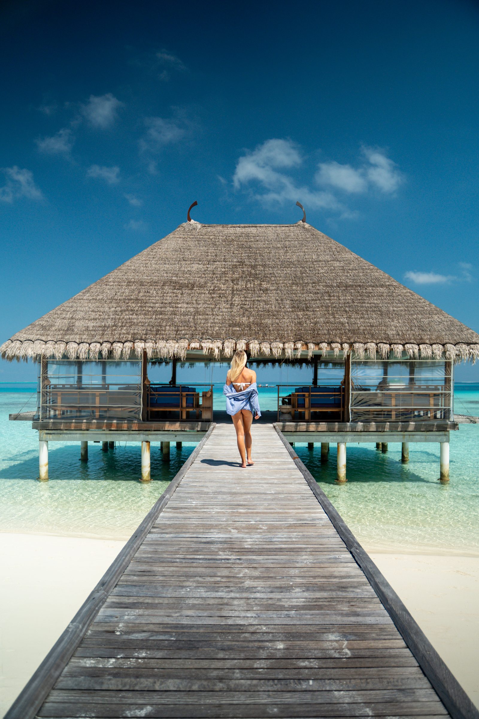 Woman walking down a jetty to a thatched overwater pavilion, Maldives