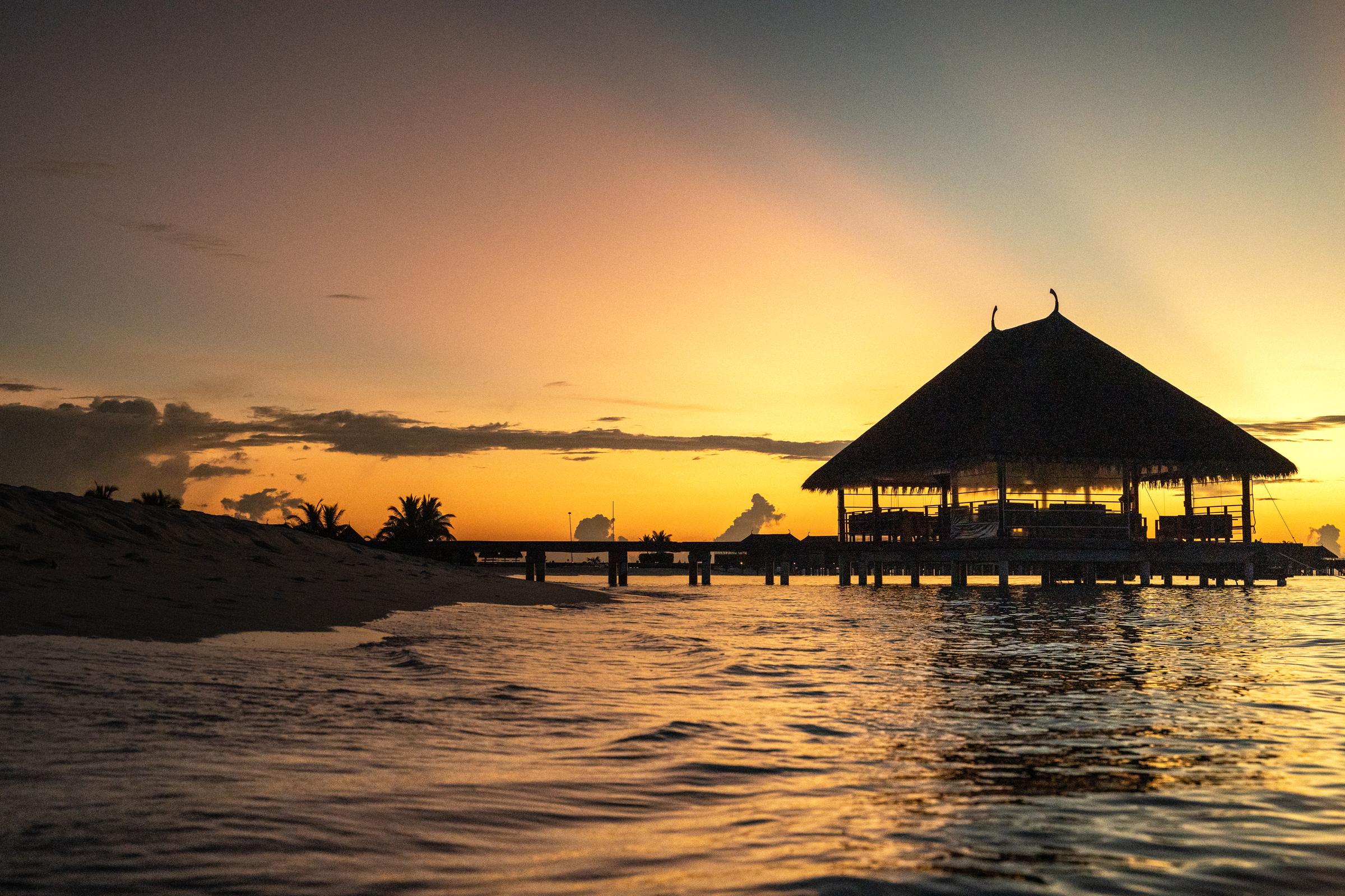 Overwater pavilion silhouetted against a golden sunset, Maldives