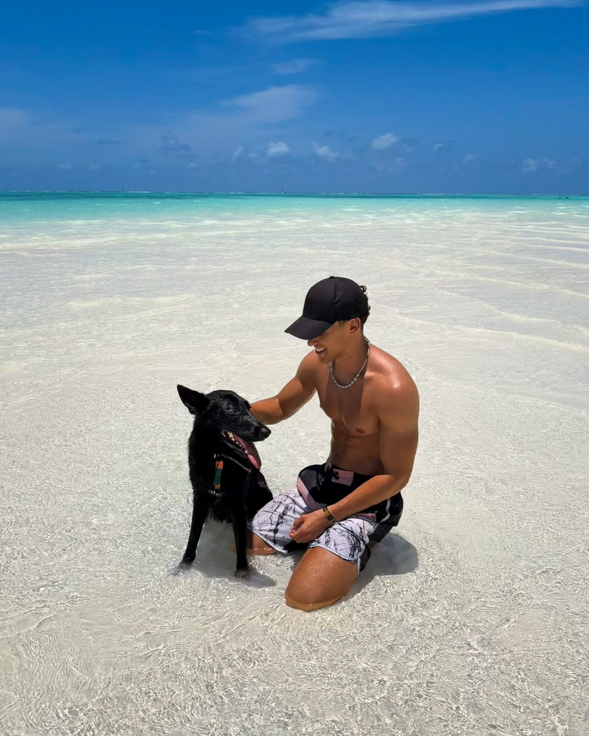 Man with a black dog on a white sand beach with turquoise water, Zanzibar